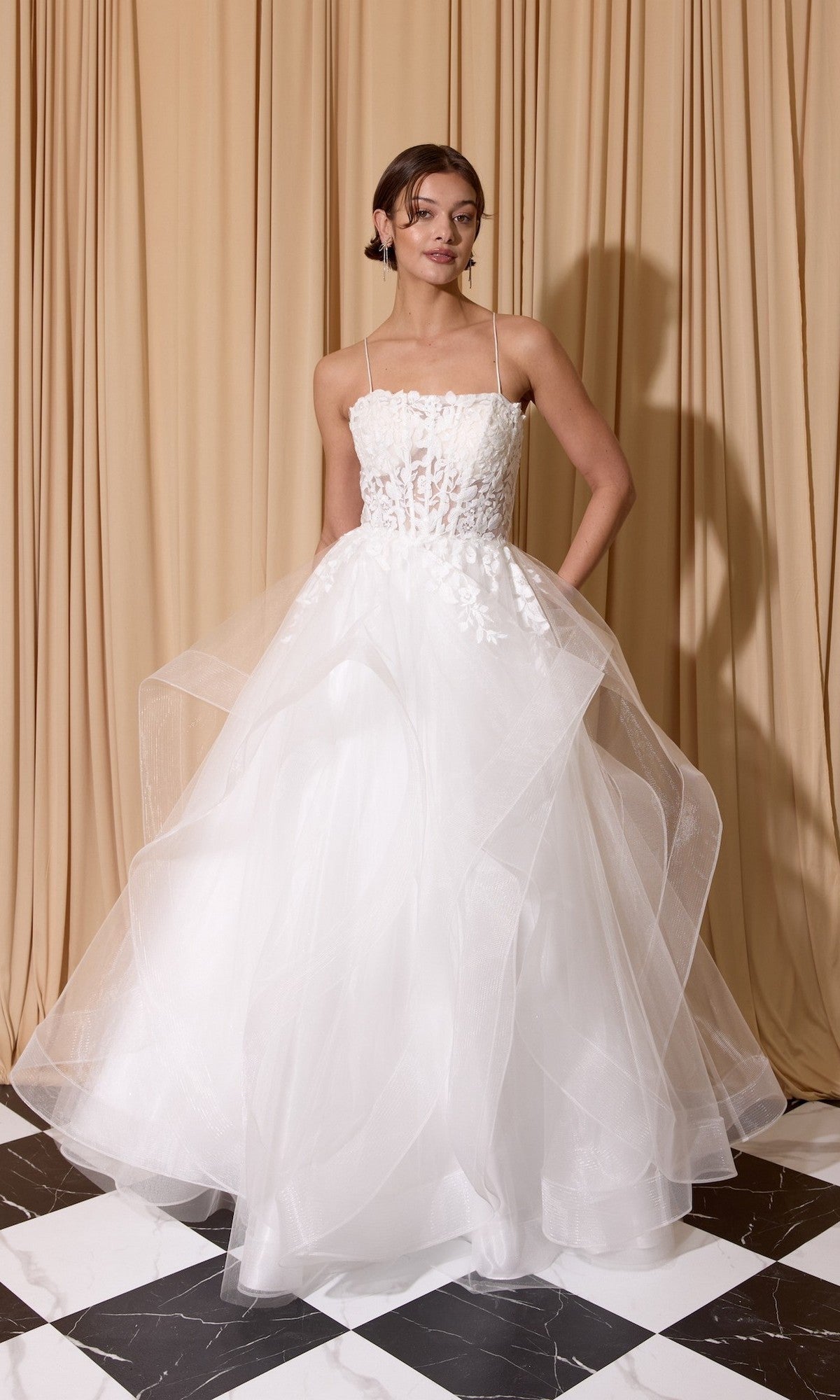 A woman wearing the off-white Long Prom Dress: Eureka EK167 stands on a black and white tiled floor in front of beige curtains.